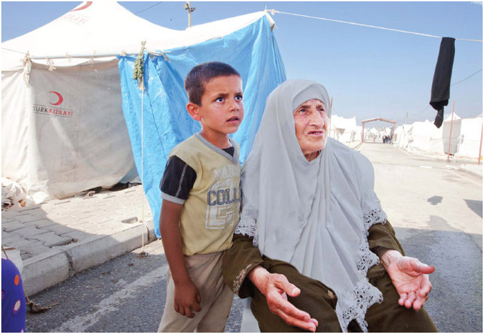 A Syrian woman and child sit outside a tent at a refugee camp on the Turkish-Syrian border. The United Nations High Commissioner for Refugees (UNHCR) estimates that of the 1.7 million Syrian refugees in Turkey in March 2015 about half are children.