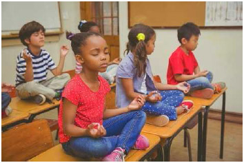 Pupils meditating in lotus position on desk in classroom at an elementary school.