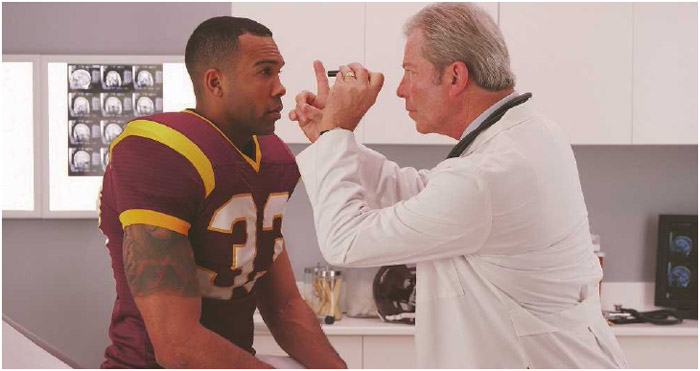 A doctor tests a football player for concussion. Playing contact sports, like football, puts athletes at a higher risk for this form of head injury. The problem was brought to light in the 2015 film Concussion, starring Will Smith.
