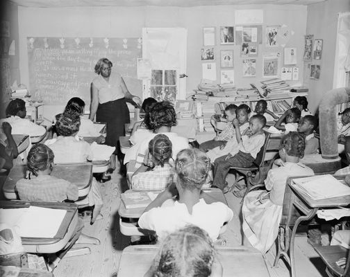 Black students attend school in a one-room shack with their teacher,  Mrs. Althea Jones.