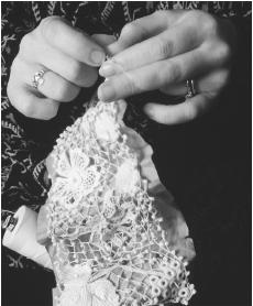 A woman makes clones knots between the main motifs in a piece of hand-crochet.