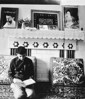 Iranian youth reads Quran at home. Framed pictures on mantle (left to right): Ayatollah Muhammad Beheshti, the Shahada, Ayatollah Ruhollah Khomeini